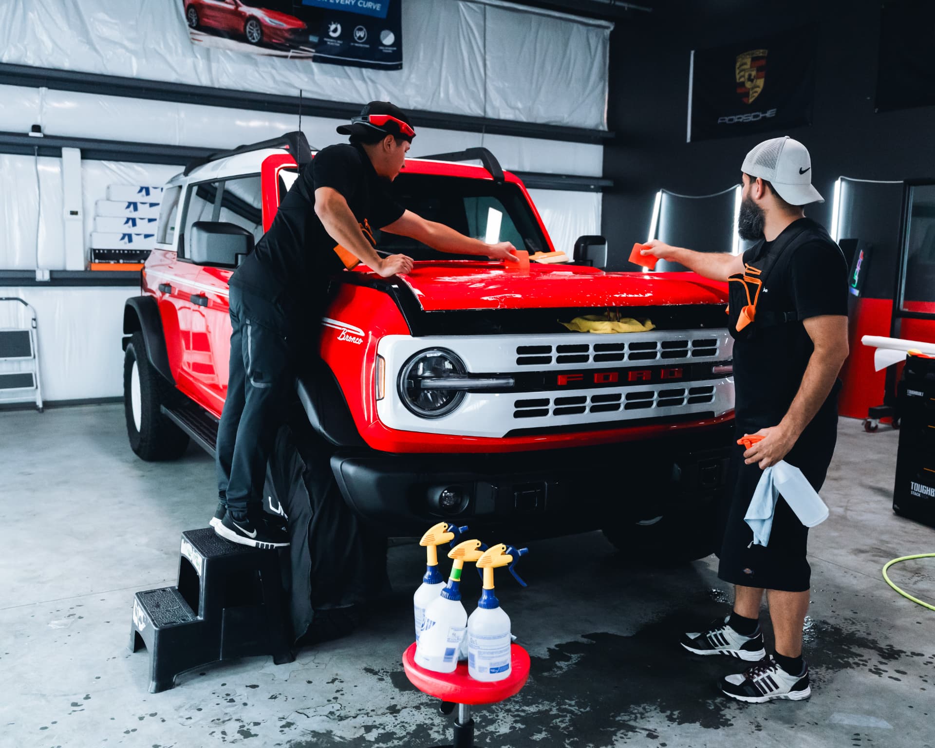 Two installers applying paint protection film to a red Bronco